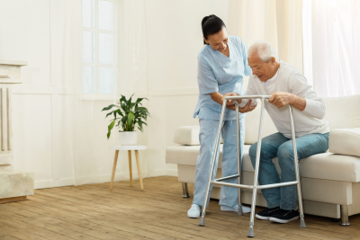 positive cheerful caregiver smiling and helping her patient to stand up
